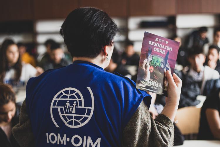 An IOM team member with an informational leaflet in front of an audience