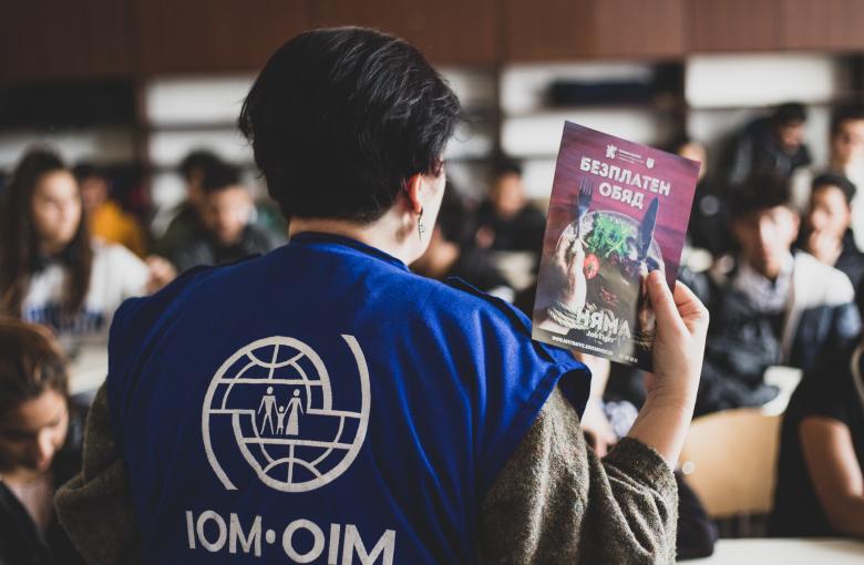 An IOM team member with an informational leaflet in front of an audience
